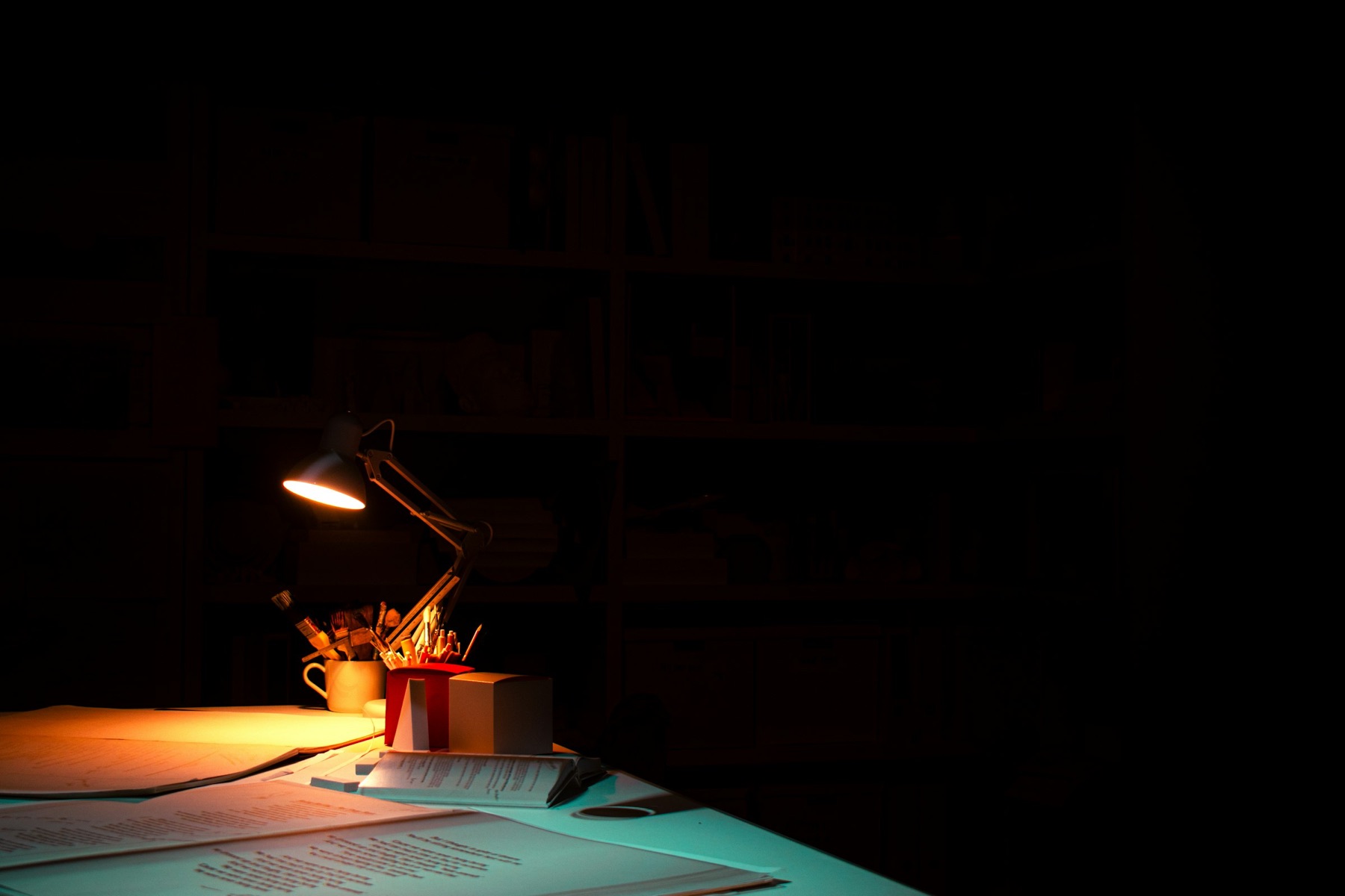 A desk lamp lit over papers in a dark room